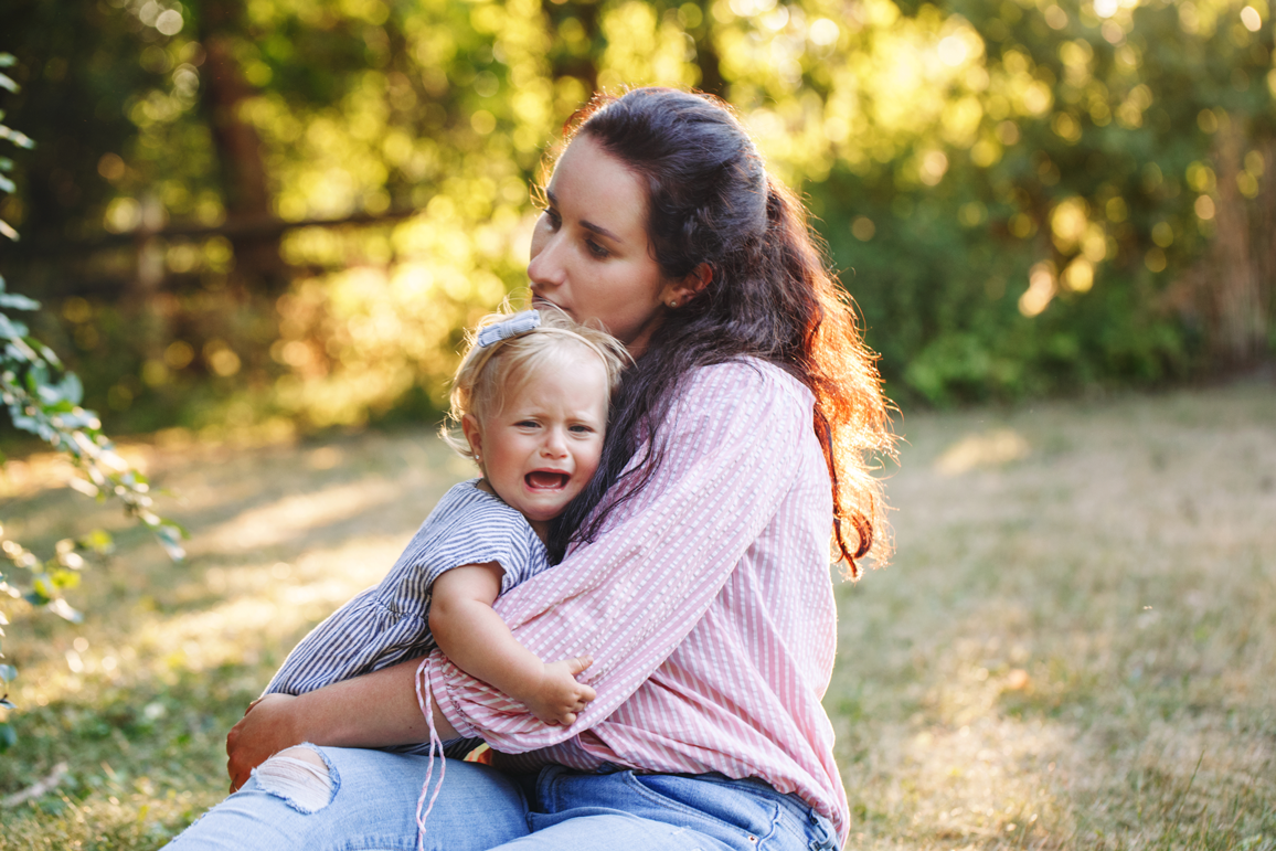 Mother comforting her crying toddler outdoors, representing family support in education.