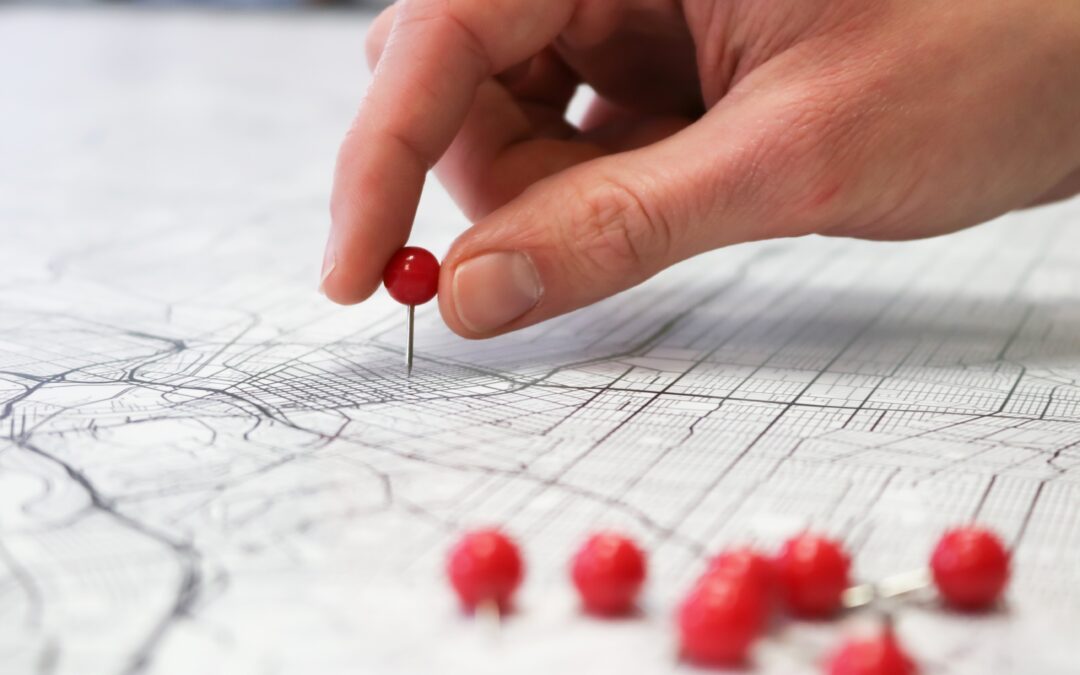 A hand places red push pins into a city street map.